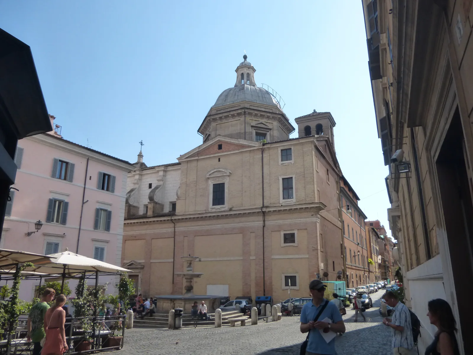 Una via del rione Monti a Roma all'incrocio con Piazza della Madonna dei Monti, tra palazzi color ocra, persiane chiuse e le insegne delle botteghe