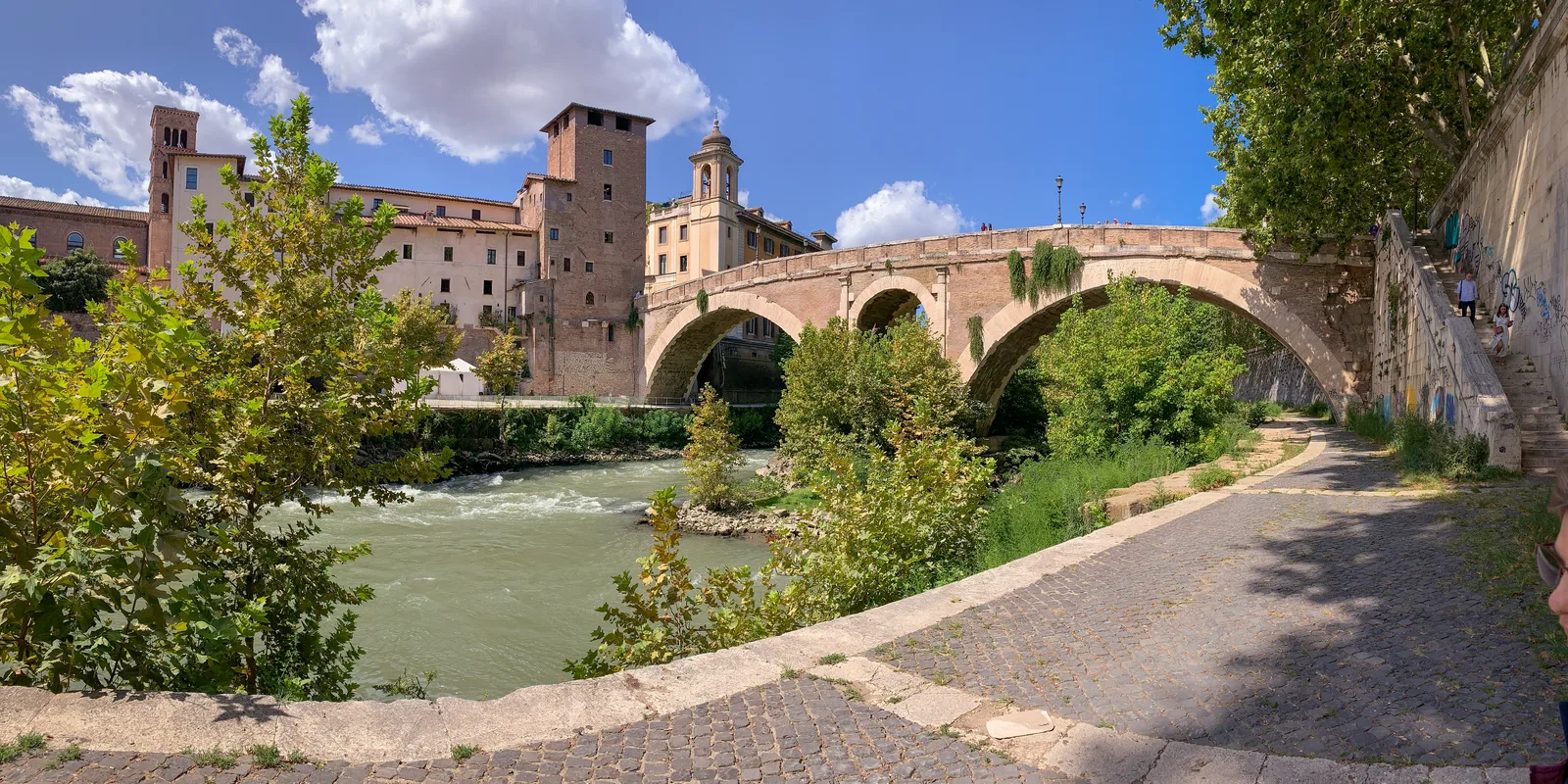 Isola Tiberina a Roma vista dal Tevere, con il Ponte Fabricio a doppia arcata in pietra che collega l'isola alla riva e il campanile di San Bartolomeo